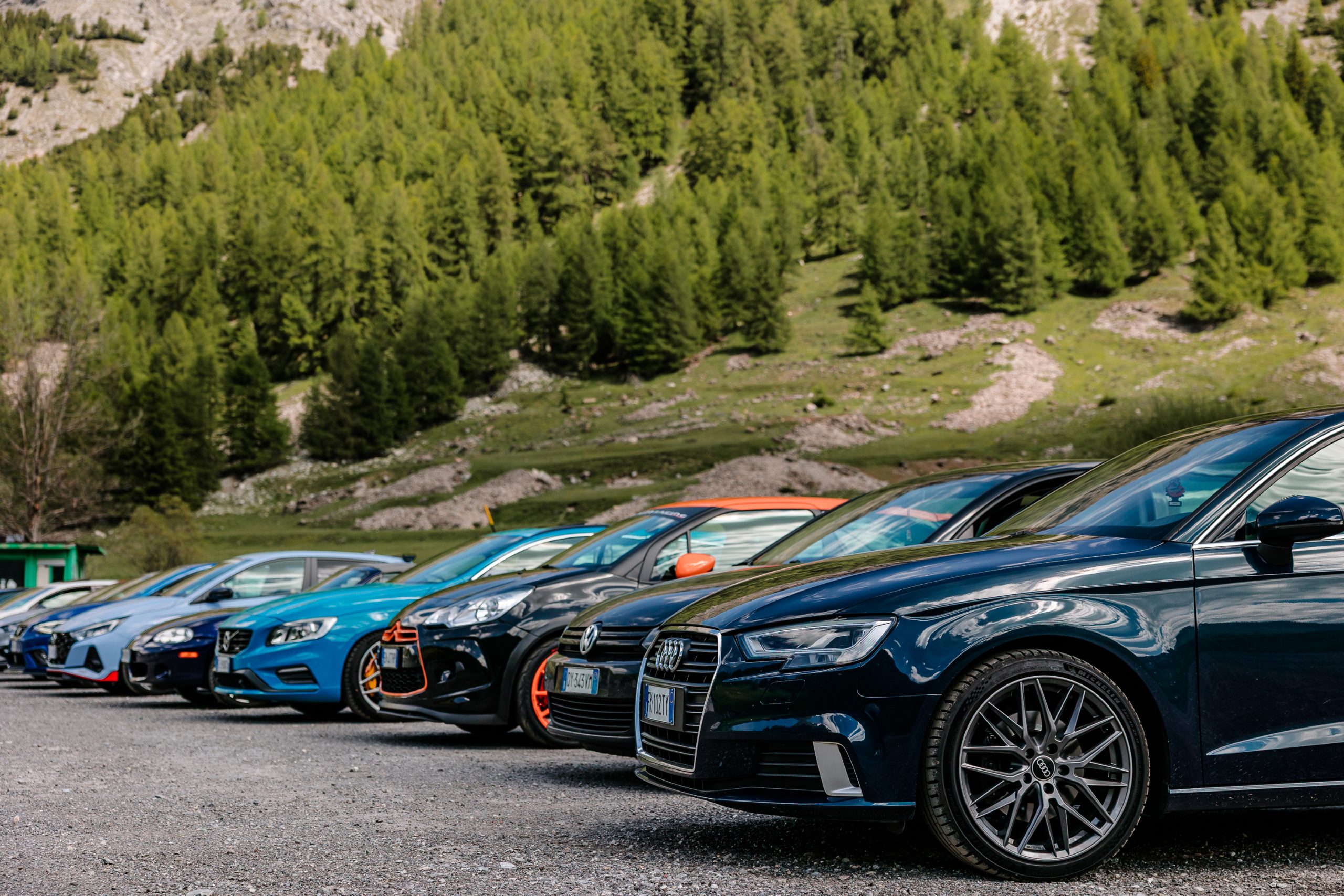Auto in fila su un piazzale di montagna, tra boschi e pareti rocciose, durante un tour di A.S.D. Cv Sc Events